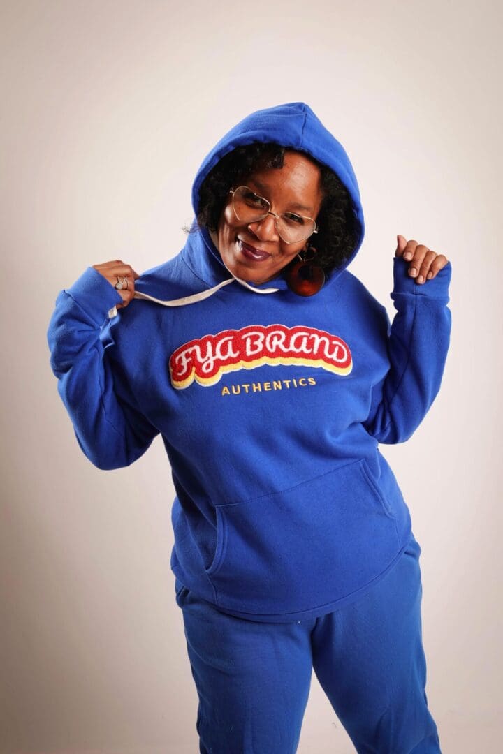 A woman in blue hoodie and pants holding onto her hood.