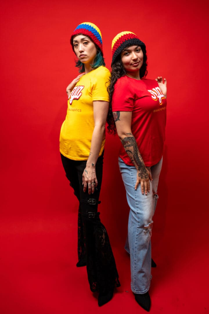 Two women posing back-to-back against a red background.
