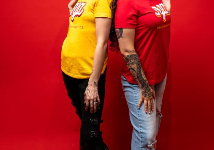 Two women posing back-to-back against a red background.